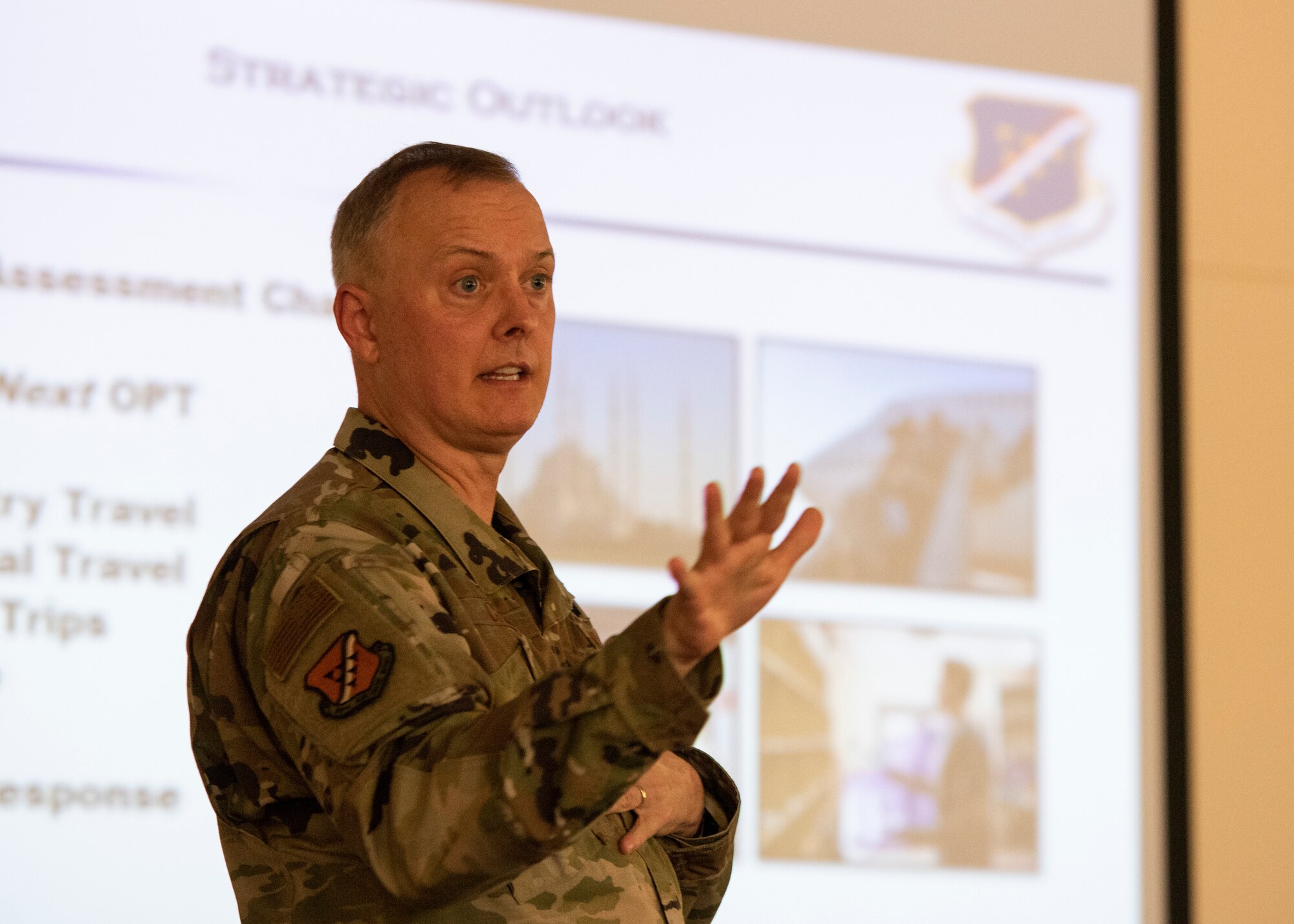 Col. John Creel, 39th Air Base Wing commander, stands in front of a projector screen and talks with gestures to an audience about the projected slide. The slide says "strategic outlook" and contains pictures from various areas.