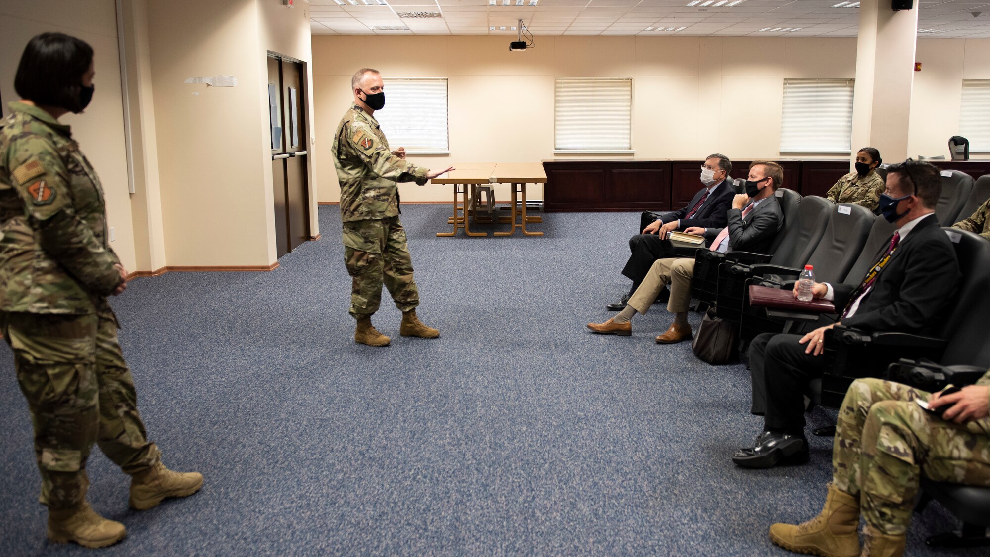 Incirlik Air Base commanders stand while talking about the base mission to visiting ambassador and his colleges in a conference room.