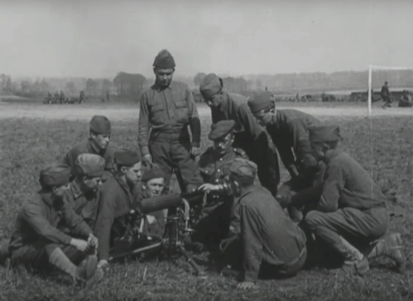 Several men surround a machine gun as they closely watch its operator.