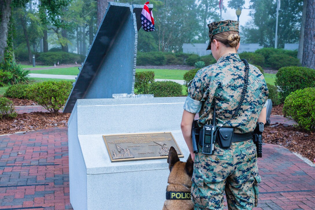 U.S. Marine Lance Cpl. Zoey Proffitt, a military working dog handler assigned to Security Company, Headquarters & Support Battalion, and military working dog Ddrago pay their respects in remembrance of the fallen heroes and victims of the events on Sept. 11, 2001 at the 9/11 Memorial in the Lejeune Memorial Gardens on Marine Corps Base Camp Lejeune, N.C., Sept. 11, 2020. The 9/11 Memorial includes a beam from the Twin Towers, presented by police and firefighters of New York in honor of the first troops deployed in the Global War on Terror from the base.