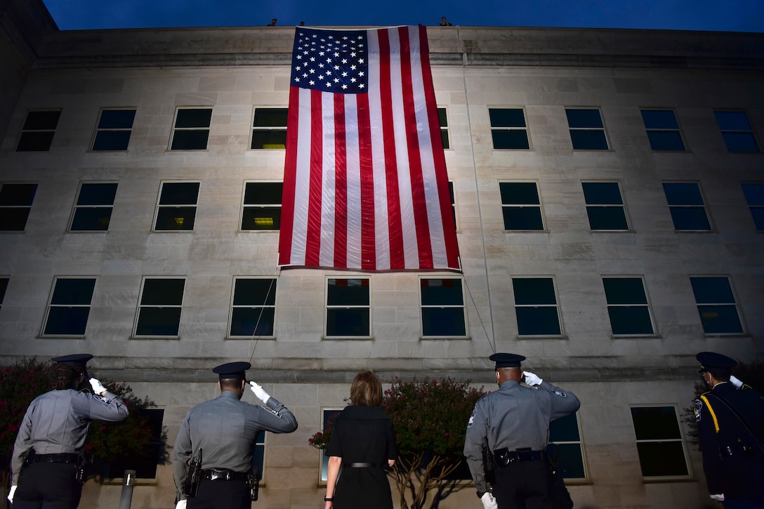 Five people seen from behind salute an American flag hanging from the Pentagon.