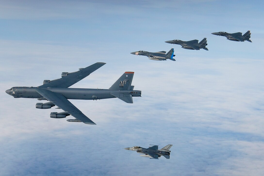 A large aircraft leads several jets flying in a V formation