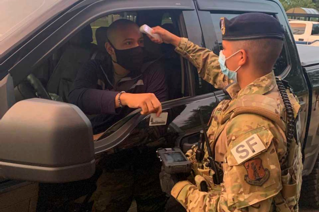 An airman checks the temperature of another airman arriving at the gate.