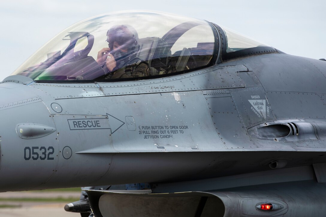 A pilot sitting inside a jet cockpit fastens his helmet.