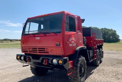 A former military truck with a red paint job sits on a gravel lot ready to help fight fires in Texas.