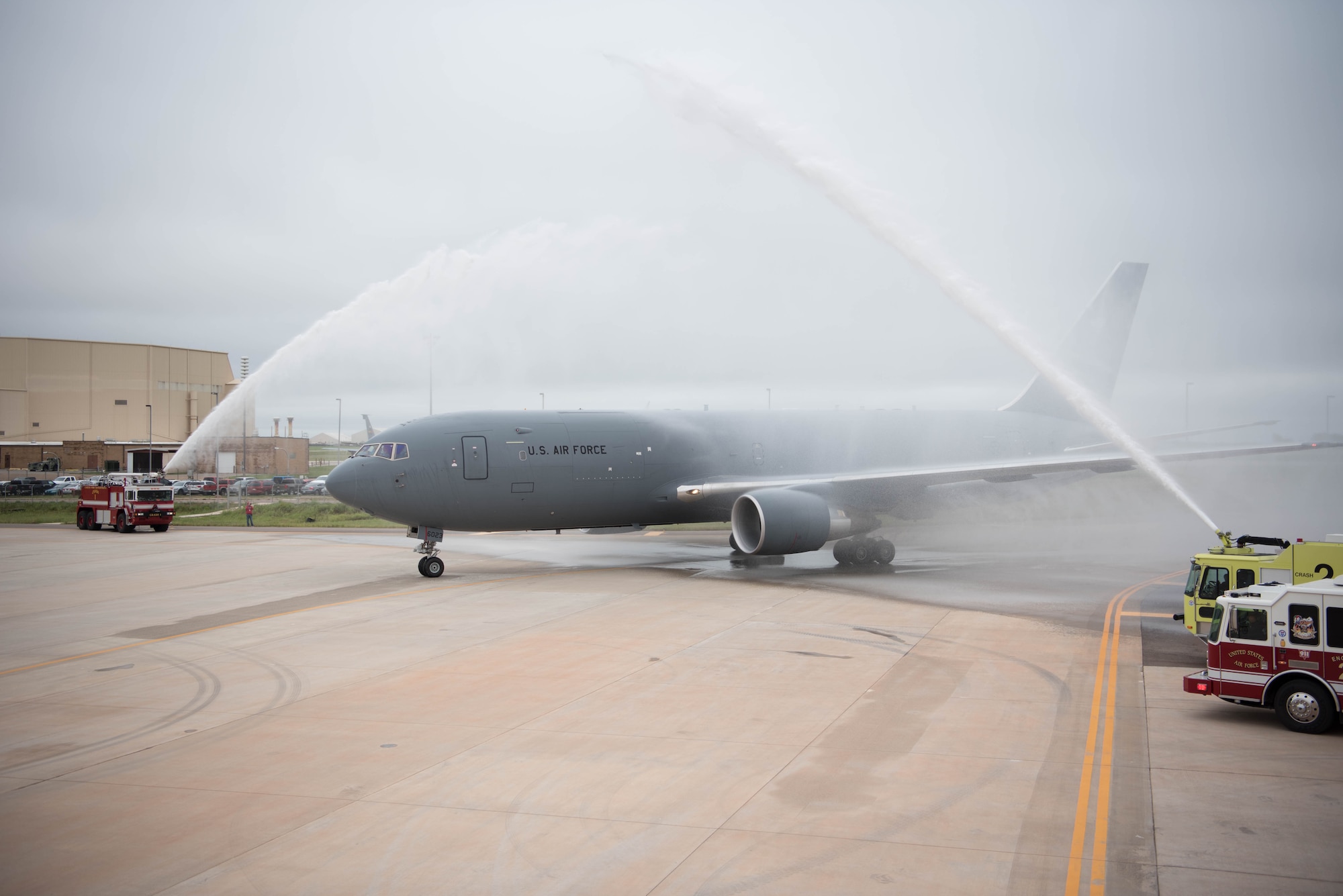 Gray airplane being sprayed by fire trucks