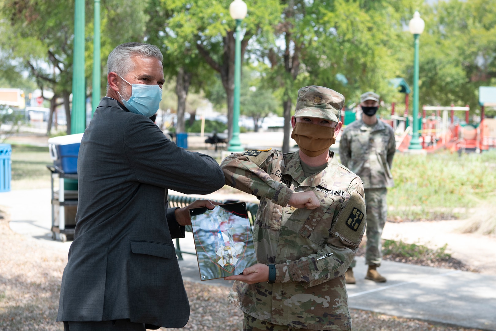 A Soldier presents a plaque to a man in a suit, both wearing masks.