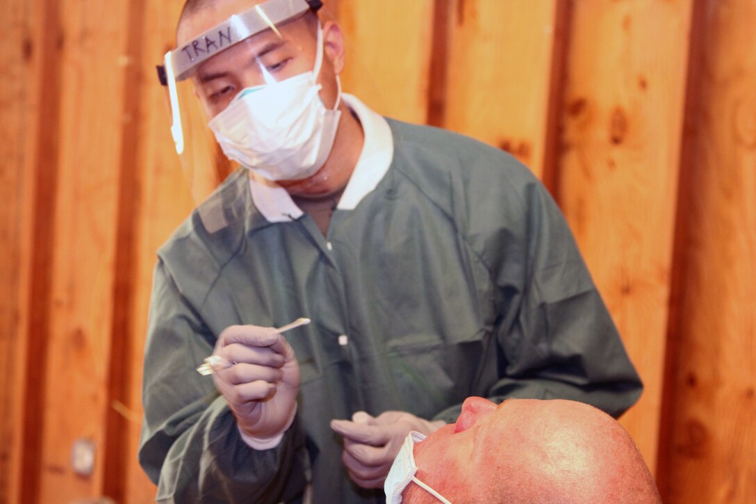 A soldier wearing personal protective equipment administers a COVID-19 nasal swab test to a soldier.