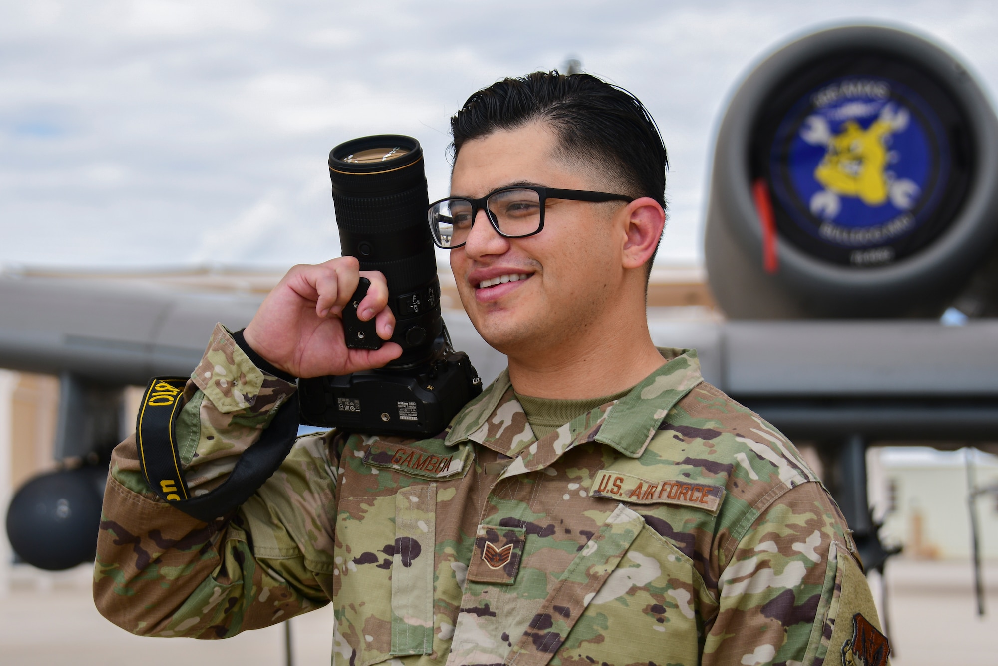 A photo of an airman standing with a camera in front of an A-10 Thunderbolt II.