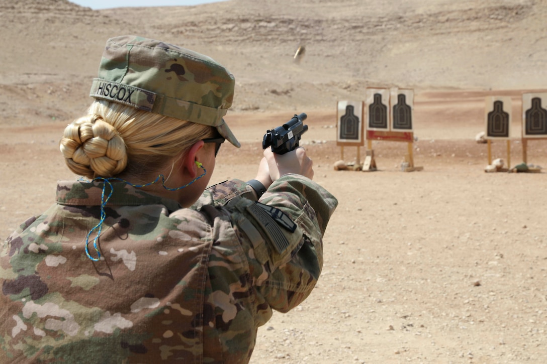 A soldier fires a weapon at a training target in a desert-like area.