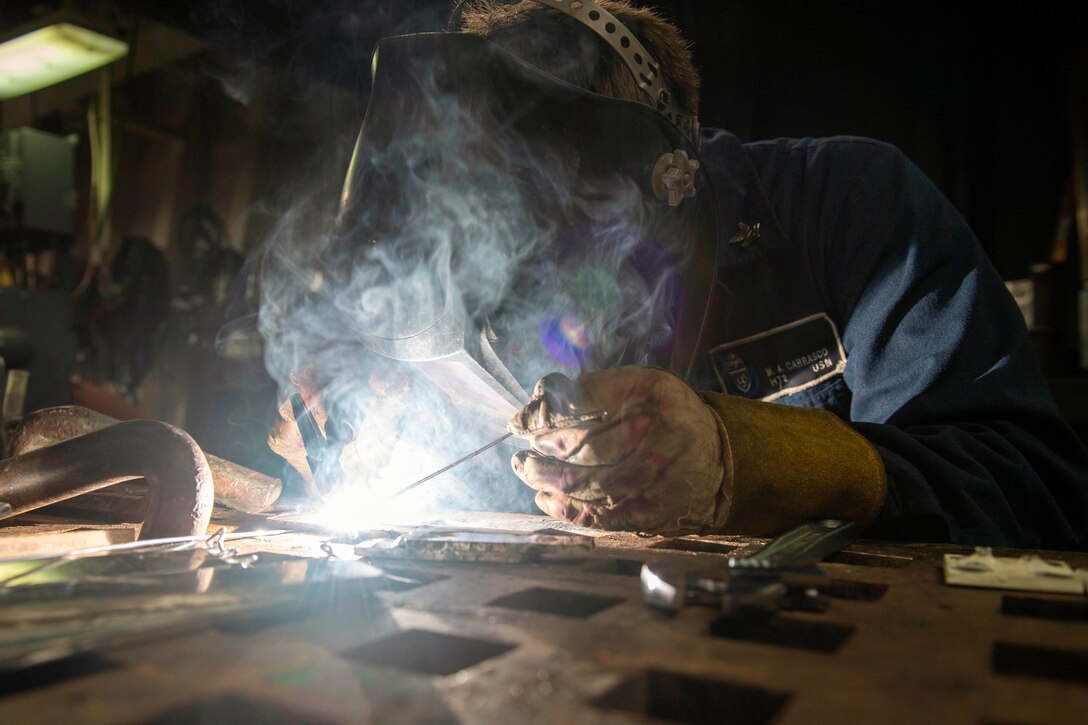 A sailor wearing protective gear performs welding work.