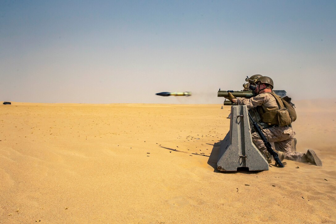 Marines fire a weapon in a desert-like area.