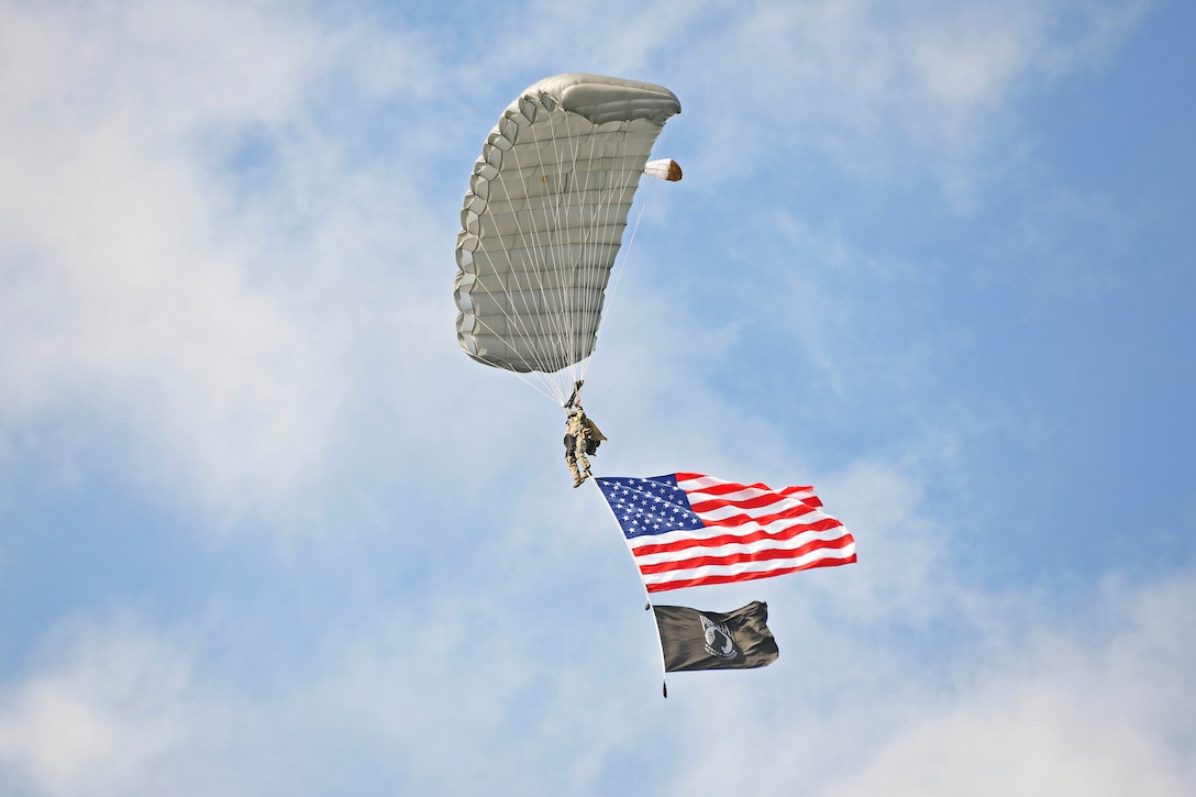 A soldier free falls wearing a parachute while flying an American Flag.