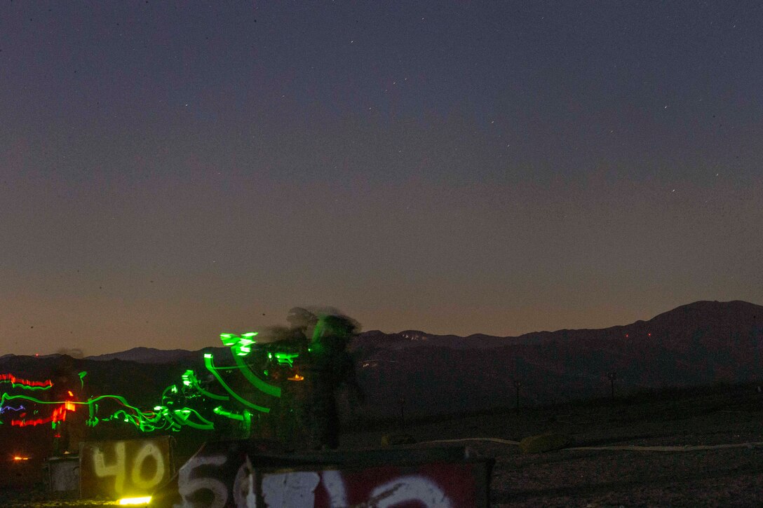 Marines hold weapons on a field at night illuminated by green light.