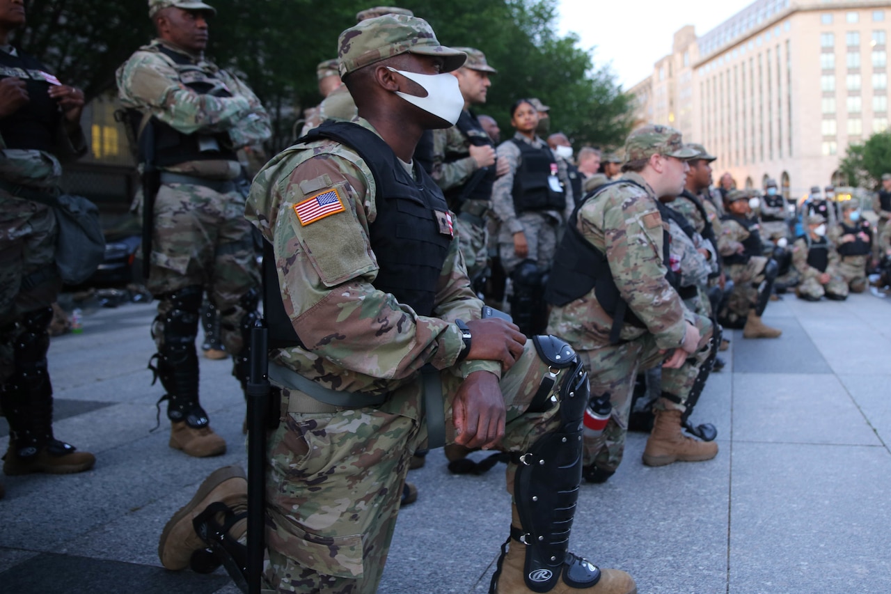 Soldiers, some kneeling and others standing, look ahead.