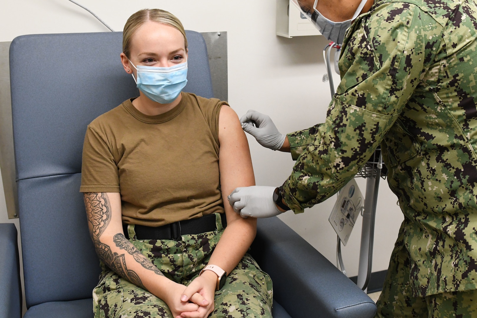 Masked Sailor cleans arm of other masked sailor to prepare for vaccine.