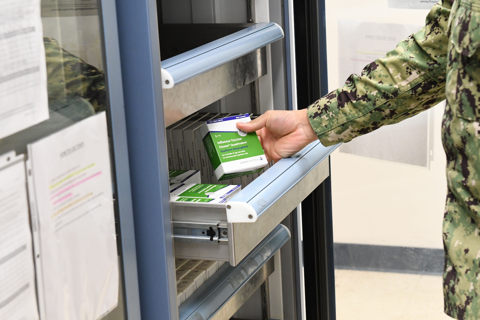 Sailor holding flu vaccine box inside vaccine refrigerator.