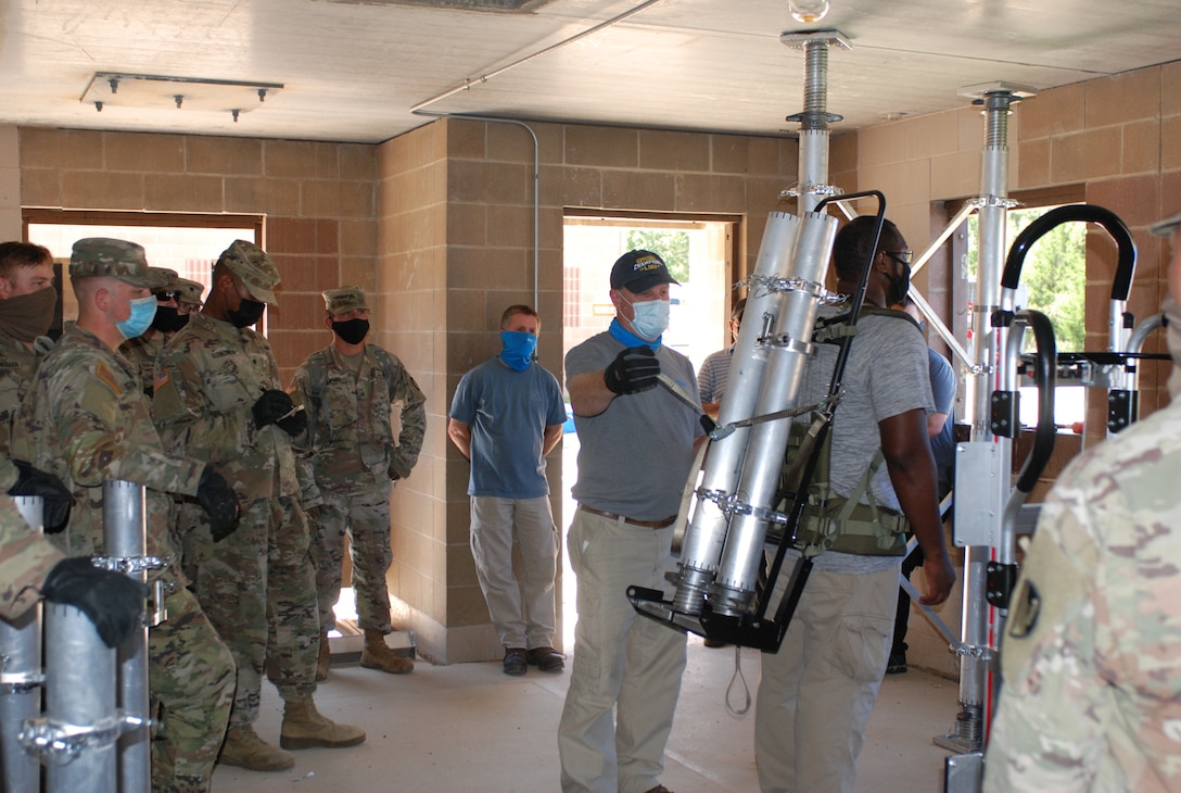 U.S. Army Engineer Research and Development Center instructors demonstrate the proper technique to safely secure and carry the pieces of the Expedient Retrofit for Existing Buildings system and quickly set it up inside an abandonded building at Training Area 230 on Fort Leonard Wood, Mo., during the Maneuver Support, Sustainment and Protection Integration Experiments-2020, or MSSPIX-20, Aug. 17, 2020.