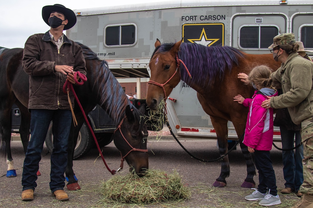 A woman and a child pet a horse while a man with a cowboy hat stands at one side.