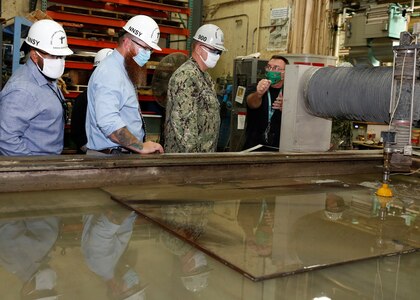 Norfolk Naval Shipyard (NNSY) Executive Development Program (EDP) Cadre 9 team members Code 105.2 Radiological Engineer Sasha Norfleet, and Code 361 Nuclear Zone Manager Aaron Jarman joined Code 300 Operations Officers Capt. Michael Oberdorf in a demonstration of the water jet cutting machine.