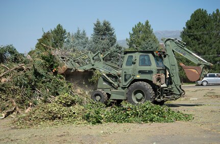 A Utah National Guard backhoe pushes tree debris into a pile at a collection point.