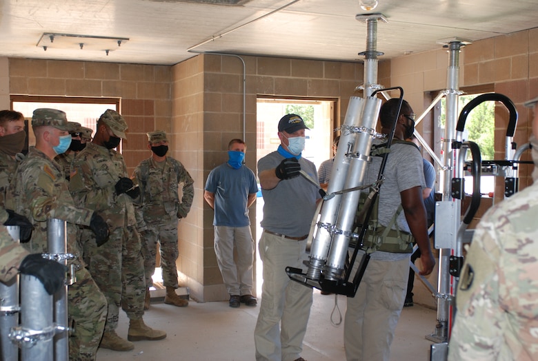 U.S. Army Engineer Research and Development Center instructors demonstrate the proper technique to safely secure and carry the pieces of the Expedient Retrofit for Existing Buildings system and quickly set it up inside an abandonded building at Training Area 230 on Fort Leonard Wood, Mo., during the Maneuver Support, Sustainment and Protection Integration Experiments-2020, or MSSPIX-20, Aug. 17, 2020.