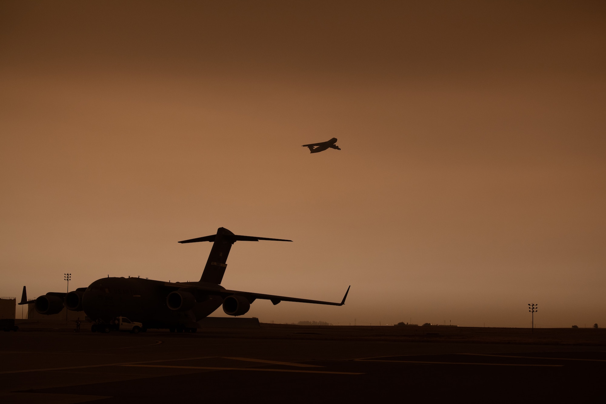 A C-5M takes off on the flight line with a yellowish, smokey sky.