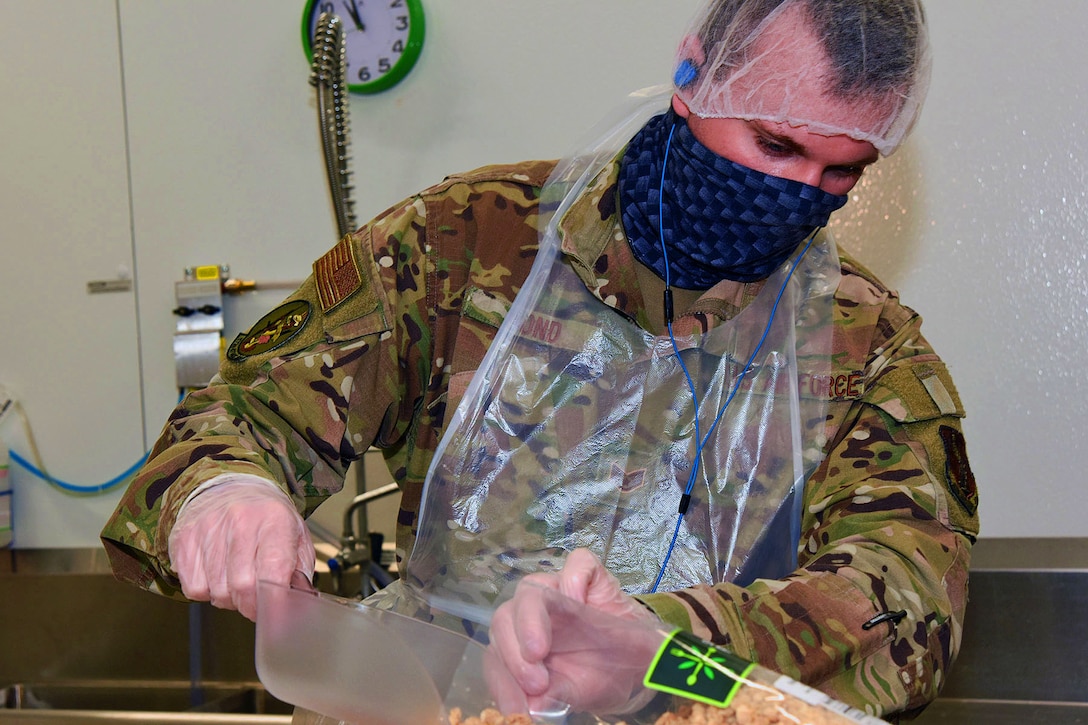 An Air National Guardsman wearing a face mask handles food.