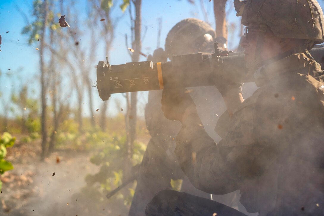 A Marine launches a rocket in a forest as other service members watch.