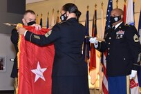 Army Medical Logistics Command Commander Brig. Gen. Michael Lalor, left, unfurls the new one-star flag with Sgt. Maj. Monnet Bushner, middle, during a promotion ceremony at Fort Detrick, Maryland, on Sept. 11. Sgt. 1st Class Brian Ockimey holds the flag staff. (Photo Credit: Ellen Crown)