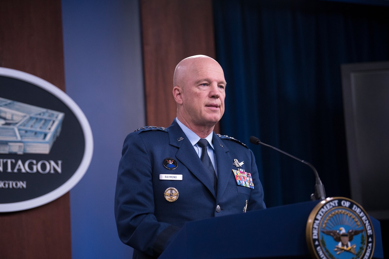 A man in military uniform stands behind a lectern.