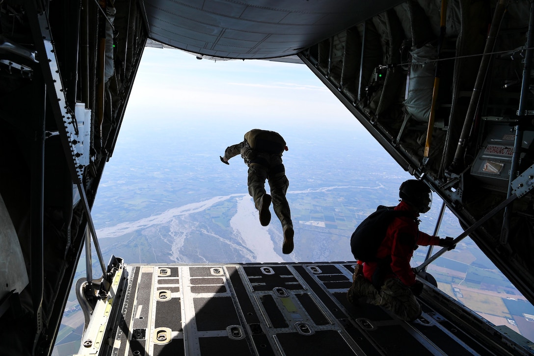 A service member jumps out the back of an aircraft.