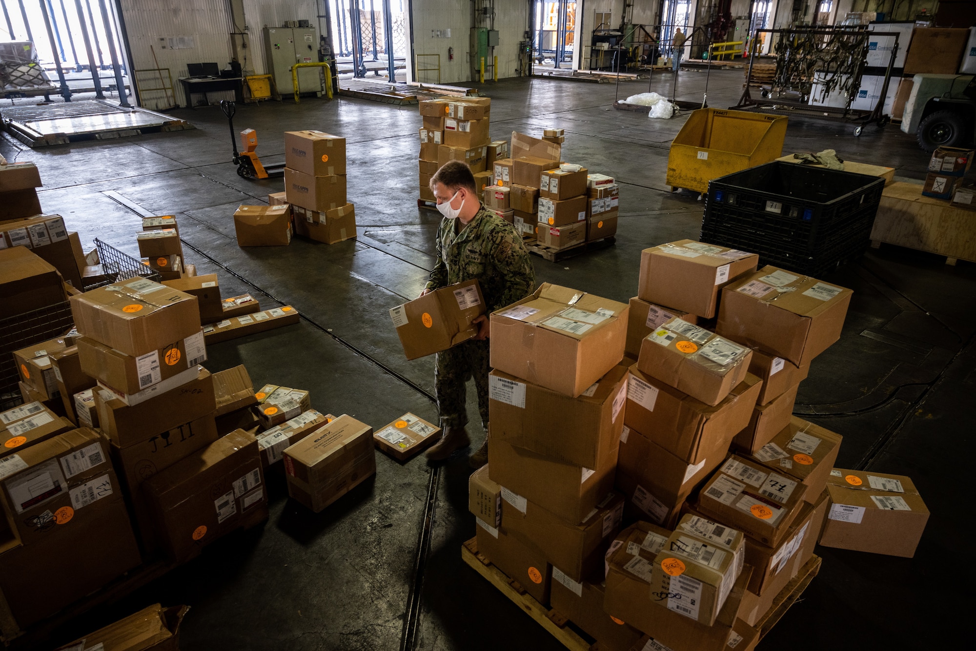 A Navy service member stacks boxes inside a large warehouse.