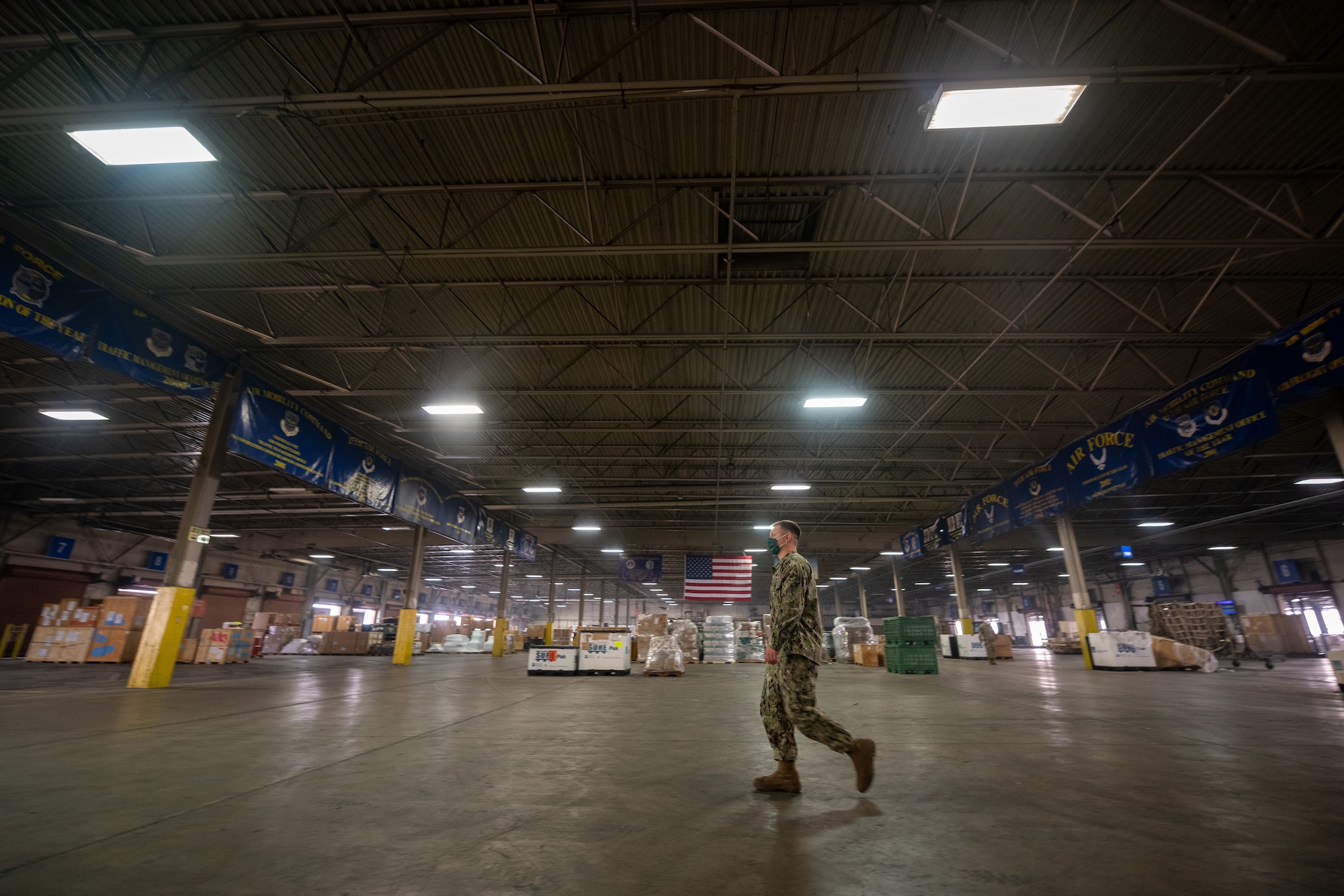 A Navy service member walks across a large warehouse floor.