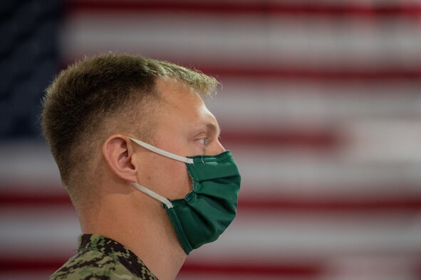 A Navy service member stands in front of a large flag.