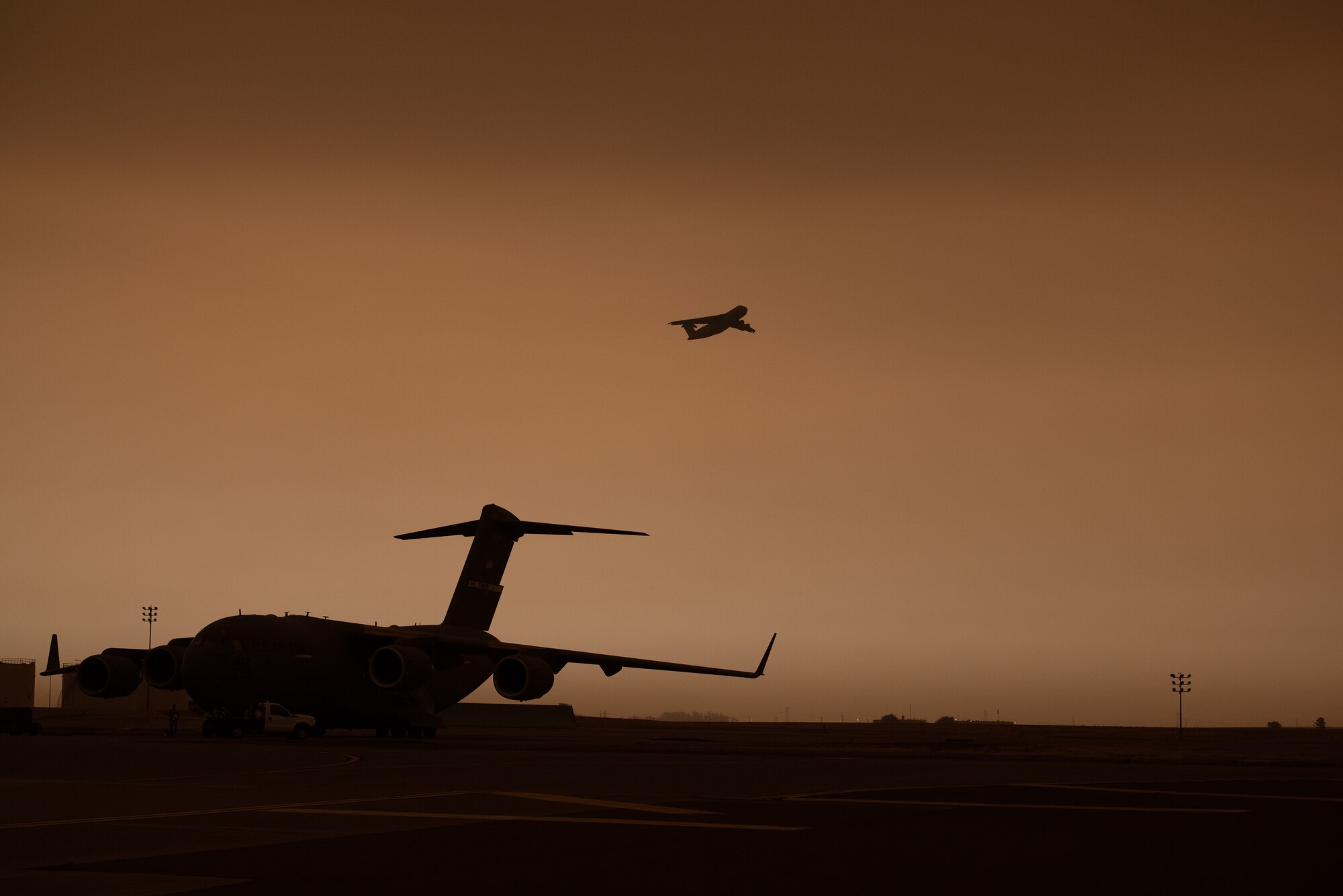 A C-5M takes off on the flight line with a yellowish, smokey sky.