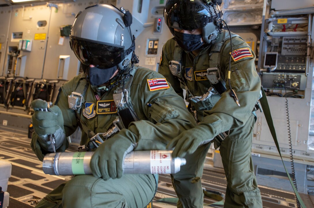 U.S. Air Force Tech Sgt. Makaio Roberts, a loadmaster assigned to the 204th Airlift Squadron, Hawaii Air National Guard, arms a flare as Master Sgt. Randy Yamada monitors for proper technique during a flare deployment training operation held Aug. 27, 2020, in Hawaii. The addition of area illuminating  flares will enhance the HIANG's continued support of astronaut rescue operations for NASA's SpaceX Human Space Flight program. (U.S. Air National Guard photo by Staff Sgt. Orlando Corpuz)