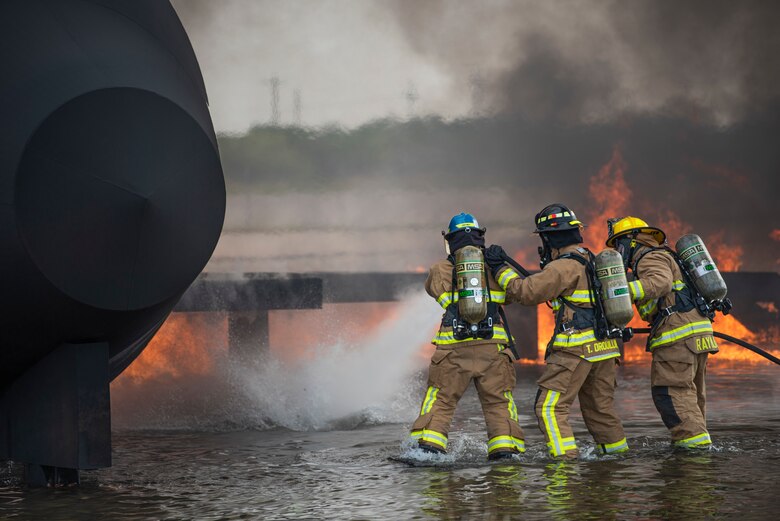 Airman Andrew Burr, 7th Civil Engineer Squadron firefighter, left, Senior Airman Thomas Drouillard, 445th CES firefighter, and Justin Raymundo, 7th CES firefighter extinguish a fire on an aircraft fire trainer at Dyess Air Force Base, Texas, Sept. 15, 2020. The liquid surrounding the aircraft fire trainer simulates jet fuel pooling around the aircraft on the tarmac during a potential real-world fire which can reach up to 1,000 degrees Fahrenheit. (U.S. Air Force photo by Airman 1st Class Colin Hollowell)