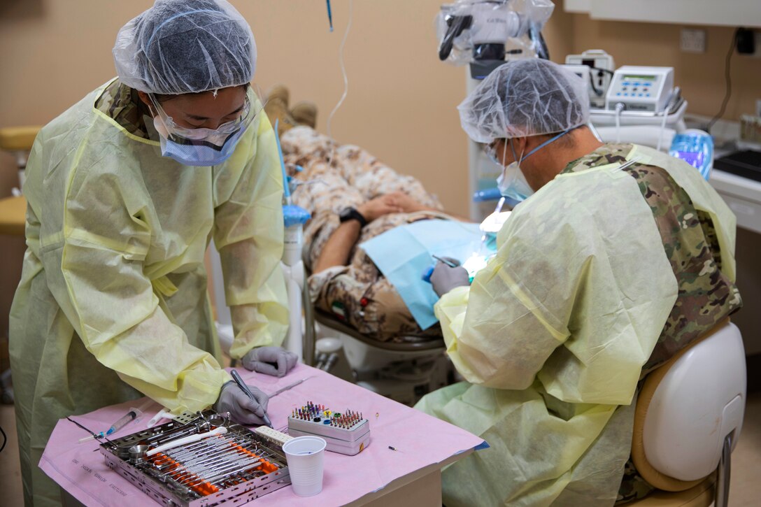 Soldiers wearing personal protective equipment perform a dental procedure.