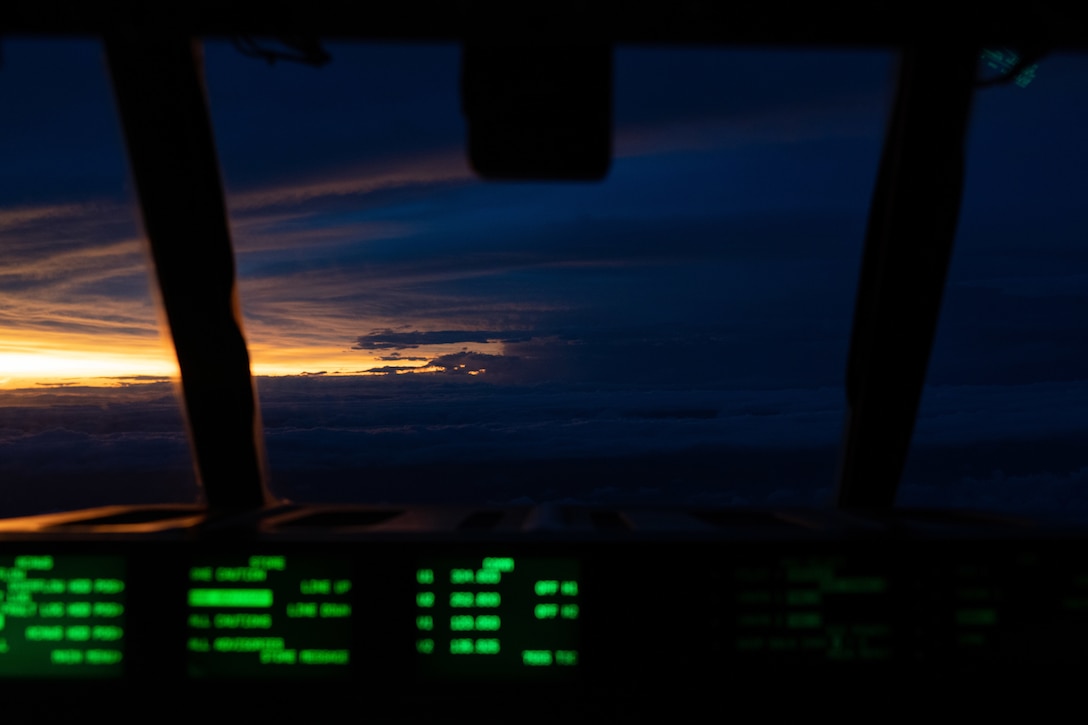 The sun shines through a sliver between dark clouds as seen from the cockpit of a military aircraft.