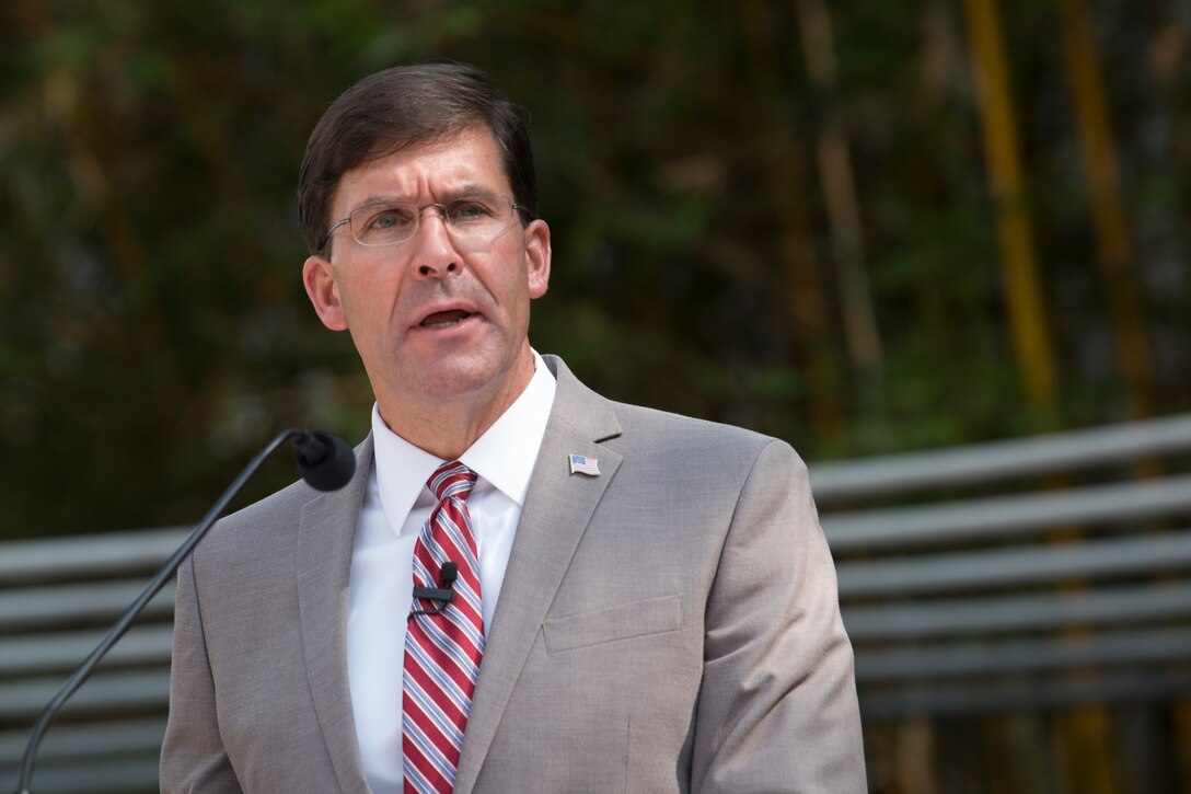 A man, standing at a microphone, speaks.