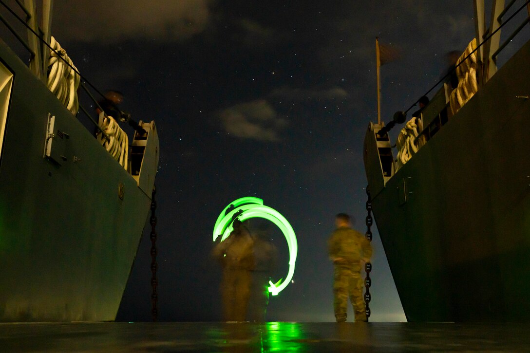 A Marine uses a green light to signal other Marines at night.