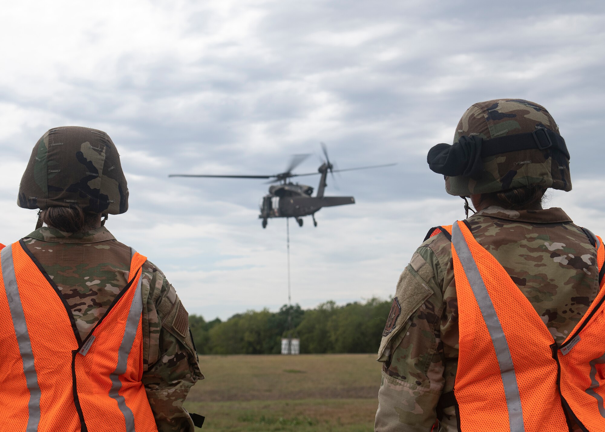 Two Soldiers watching a helicopter lift equipment.