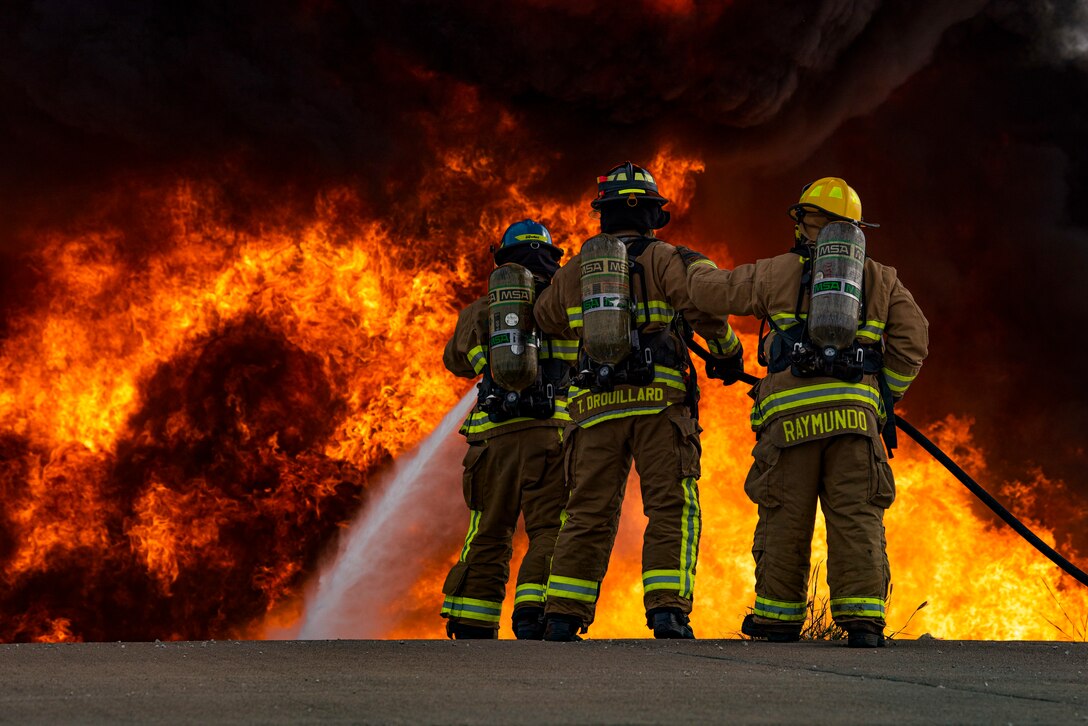 Airman Andrew Burr, 7th Civil Engineer Squadron firefighter, left, Senior Airman Thomas Drouillard, 445th CES firefighter, and Justin Raymundo, 7th CES firefighter extinguish a fire on an aircraft fire trainer at Dyess Air Force Base, Texas, Sept. 15, 2020. The firefighters tested a new ultra-high pressure fire hose that sprays a mist intended to cool the gasses surrounding the flames; earlier models typically blanket the flames with larger water droplets. (U.S. Air Force photo by Airman 1st Class Colin Hollowell)