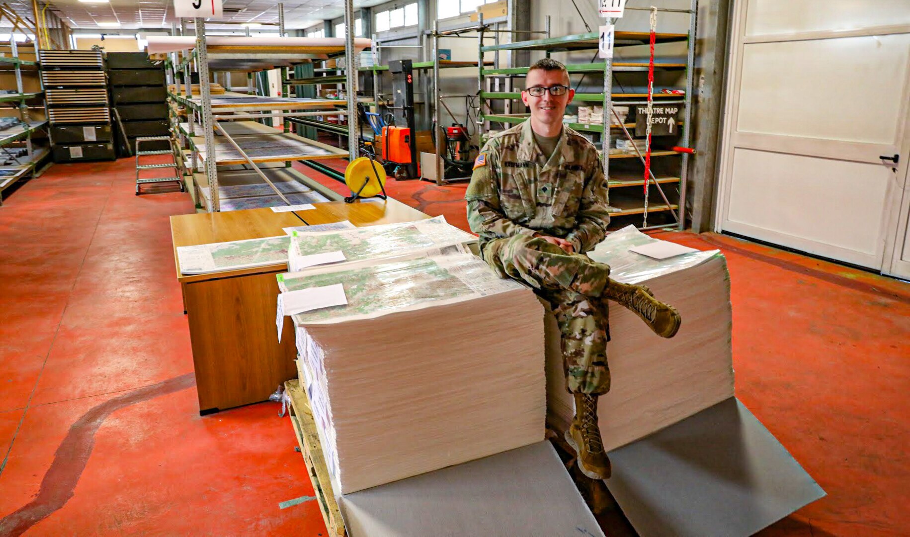 Spc. Caleb Kaufmann, a geospatial engineer Soldier with the 41st Infantry Brigade Combat Team, Oregon National Guard, deployed to the KFOR Regional Command East mission sits on a stack of maps in the map depot Sept. 1, 2020, at Camp Film City, Pristina/Prishtina Kosovo. Kaufmann was the sole continuity between the outgoing Czech Republic NATO partners and incoming Austrian NATO partners in a warehouse with over 100,000 maps.