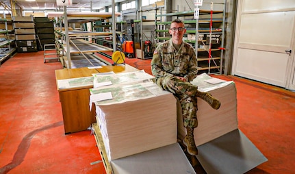 Spc. Caleb Kaufmann, a geospatial engineer Soldier with the 41st Infantry Brigade Combat Team, Oregon National Guard, deployed to the KFOR Regional Command East mission sits on a stack of maps in the map depot Sept. 1, 2020, at Camp Film City, Pristina/Prishtina Kosovo. Kaufmann was the sole continuity between the outgoing Czech Republic NATO partners and incoming Austrian NATO partners in a warehouse with over 100,000 maps.