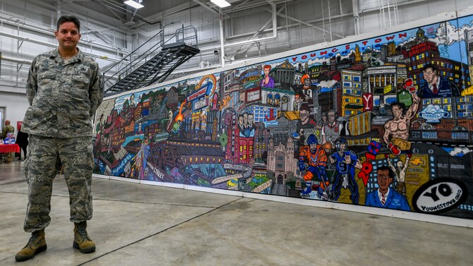 Master Sgt. Bob Barko Jr., the superintendent of the 910th Airlift Wing public affairs office, poses for a photo with his giant mural of Youngstown, Ohio, pop culture, Jan. 11, 2020, at Youngstown Air Reserve Station's Career and Diversity Day.  The purpose of the Career and Diversity Day was to bring together the unique differences of Airmen to form a valued organization where Airmen know they can prosper and continue to serve with pride.
