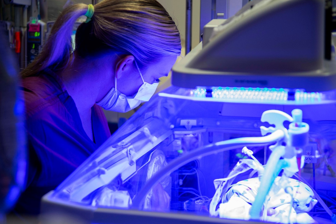 A nurse wearing personal protective equipment conducts a morning assessment on an infant in the hospital's NICU.