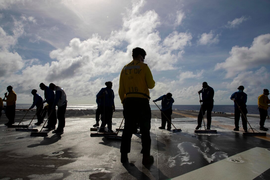 A group of sailors wash the flight deck of a ship.