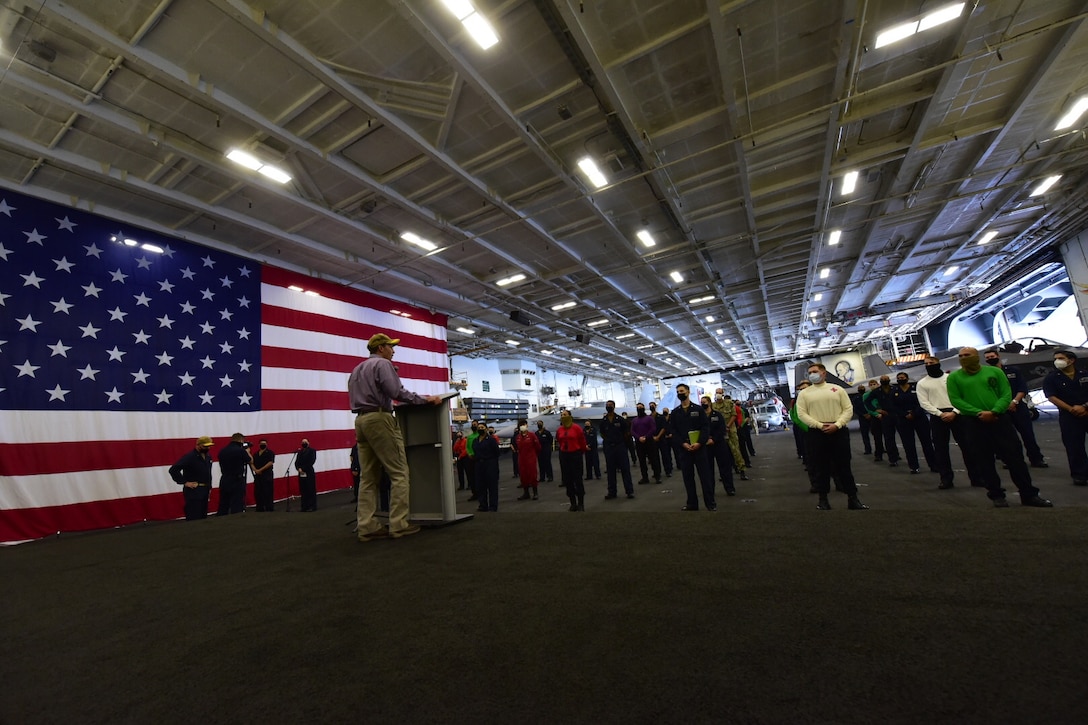 The defense secretary speaks to a group of sailors in a hangar bay on a ship.